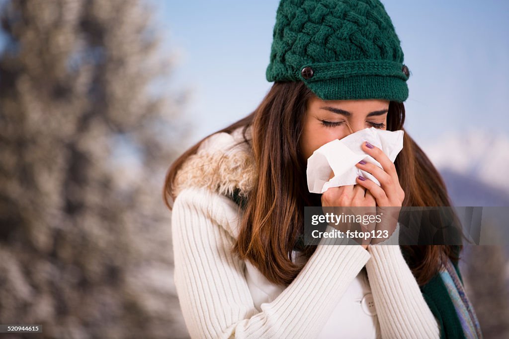 Latin woman with flu or allergies sneezes while outside. Winter.