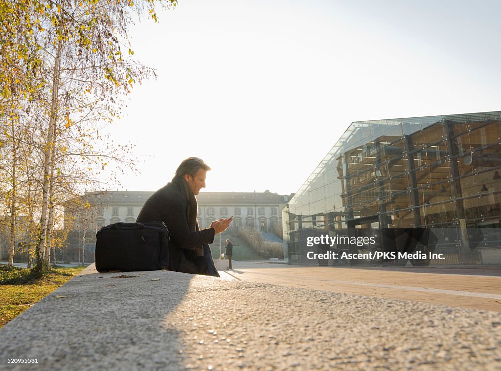 Businessman pauses to send text near office