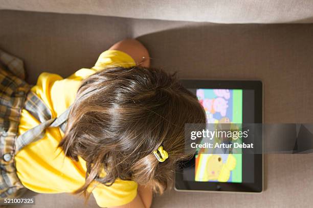 Girl watching cartoons online with the iPad tablet laying in the sofa at home with view from above.