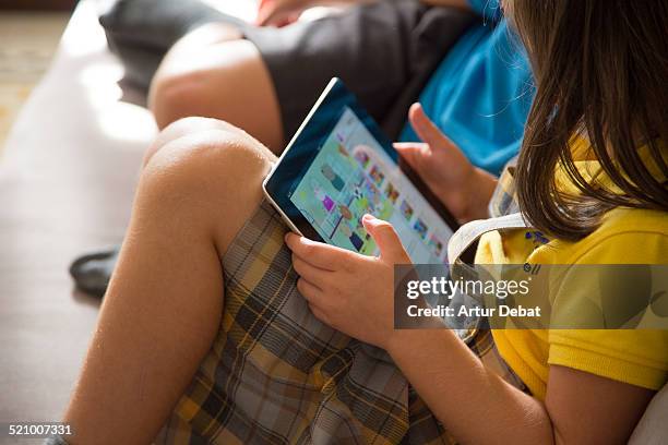 Boy and girl watching cartoons online with the iPad tablet sitting in the sofa at home.