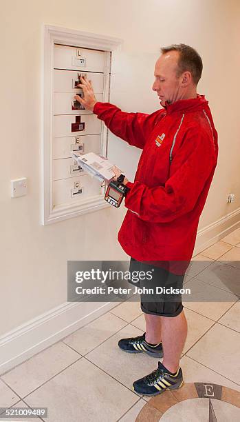 British Postman is delivering mail to mailboxes in the wall of an apartment block in Nottingham, UK.
