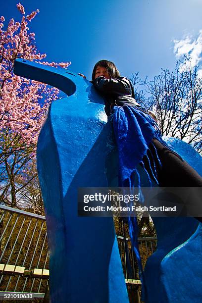 Asian woman riding a blue, wooden horse in the Hakone Open Air Museum, a very popular sightseeing spot for visiting tourists.