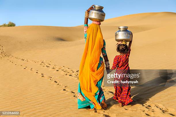 indische frau mit kleinen tochter, die wasser von gut - rajasthani women stock-fotos und bilder