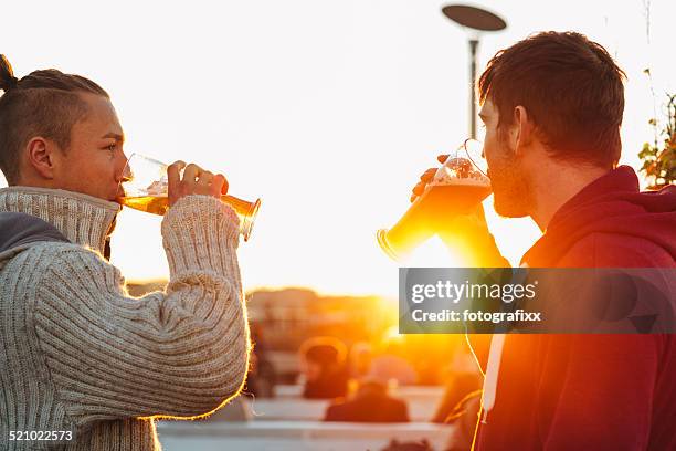 handsome young men drinking beer in front of backlit - witbier stockfoto's en -beelden