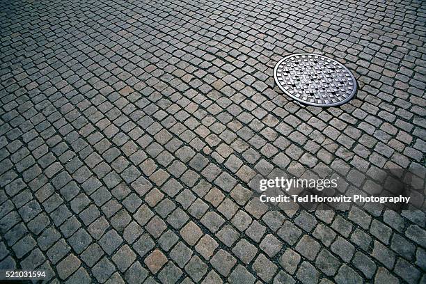 manhole cover on cobblestone path - マンホール ストックフォトと画像