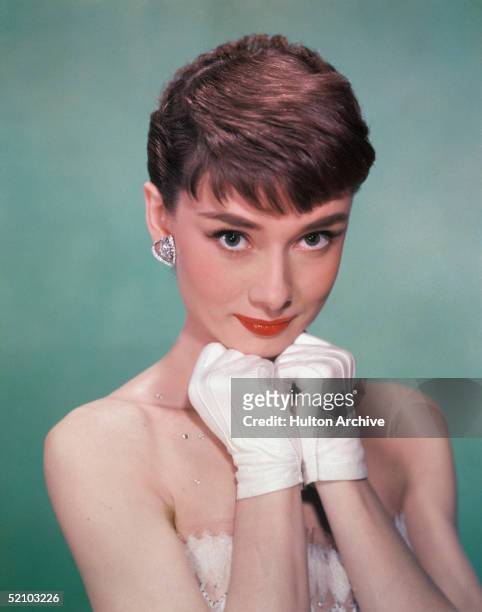 Portrait of Belgian-born American actress Audrey Hepburn as she wears a strapless gown and holds white kid-gloved hands up to her chin, early 1950s.