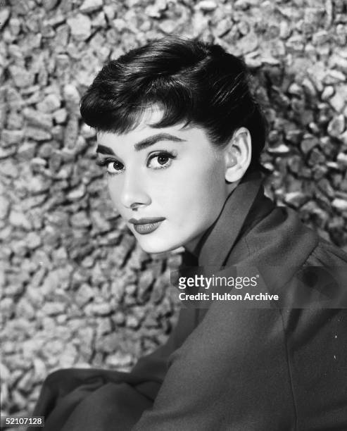 Portrait of Belgian-born American actress Audrey Hepburn as she sits by a stone wall, early 1950s.