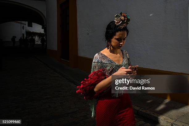 Woman wearing a traditional Sevilla dress checks her mobile phone as she walks past the main entrance of La Maestranza bullring ahead of a bullfight...