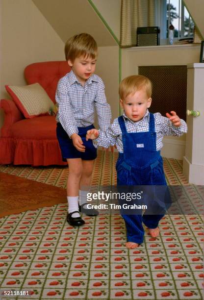 Prince William Standing Behind His Brother, Prince Harry, To Help Him As He Tries To Walk On His Own In The Playroom At Kensington Palace