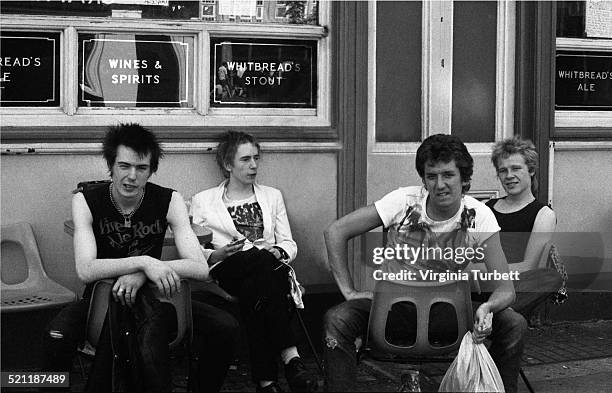 The Sex Pistols sit outside a pub during a break from recording a video for the song 'Pretty Vacant', London, June 1977. L-R Sid Vicious, Johnny...