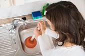 Woman Using Plunger In Sink