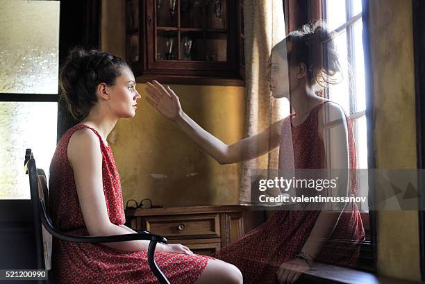 pensive young woman looking throuth the window - schizofrenie stockfoto's en -beelden