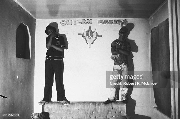 Portrait of two unidentified members of Bronx street gang the Outlaw Makers as they stand on a couch in their clubhouse, New York, New York, 1975.