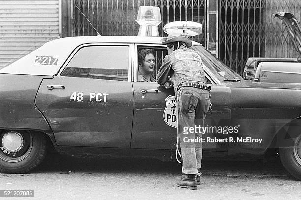 Member of Bronx street gang the Dragons leans against the passenger door of a police car to speak with an officer, New York, New York, 1975.
