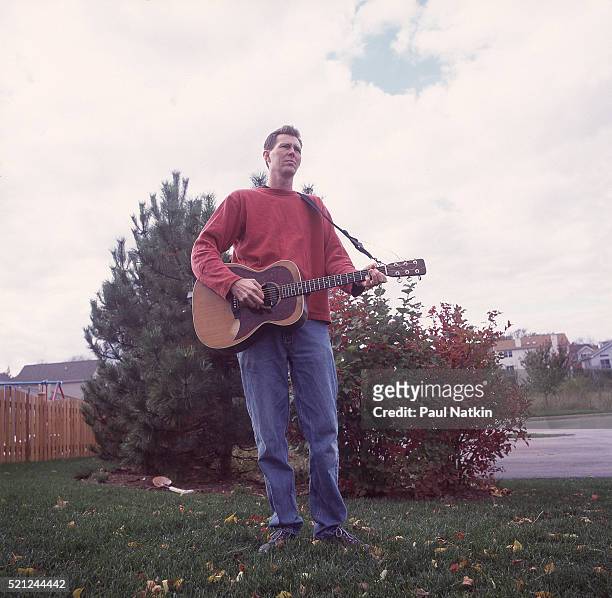 Portrait of American Country musician Robbie Fulks as he poses with his guitar outside his home, Chicago, Illinois, June 15, 2000.