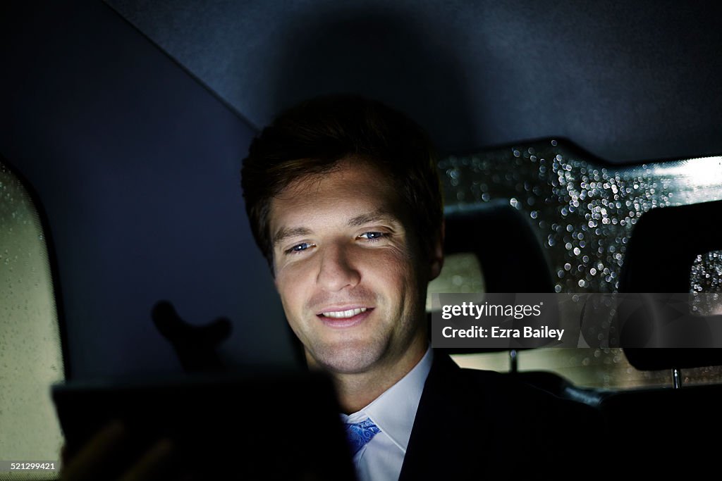 Businessman uses a tablet in a taxi, at night.