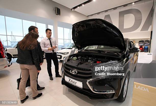 Salesman, right, shows customers a new Lada X-Ray automobile, manufactured by AvtoVAZ OAO, in the showroom of a Lada car dealership in Izhevsk,...