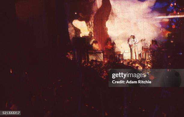 View from the back of the venue showing the crowd at the Roundhouse watching Pink Floyd perform in front of a psychedelic light show projection,...