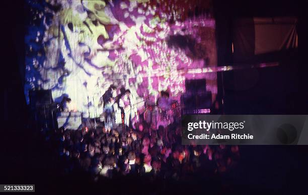 View from the back of the venue showing the crowd at the Roundhouse watching Pink Floyd perform in front of a psychedelic light show projection,...