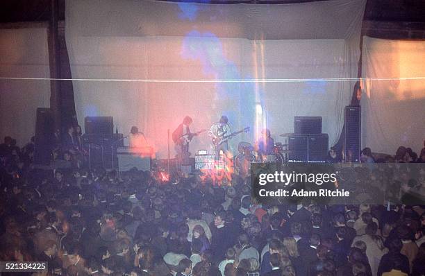 View from the back of the venue showing the crowd at the Roundhouse watching Pink Floyd perform in front of a psychedelic light show projection,...