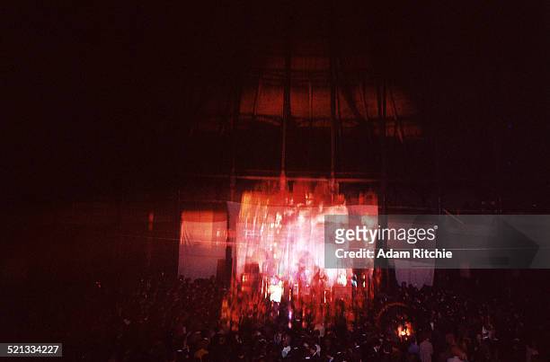 View from the back of the venue showing the crowd at the Roundhouse watching Pink Floyd perform in front of a psychedelic light show projection,...