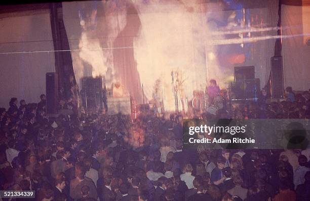 View from the back of the venue showing the crowd at the Roundhouse watching Pink Floyd perform in front of a psychedelic light show projection,...