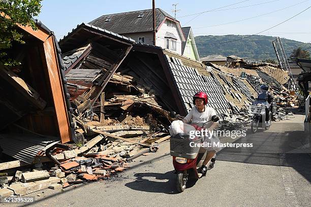 Woman rides a scooter in front of a collapsed house a day after the 2016 Kumamoto Earthquake on April 15, 2016 in Mashiki, Kumamoto, Japan. As of...