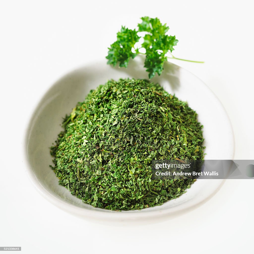 A bowl of dried parsley with fresh parsley leaf