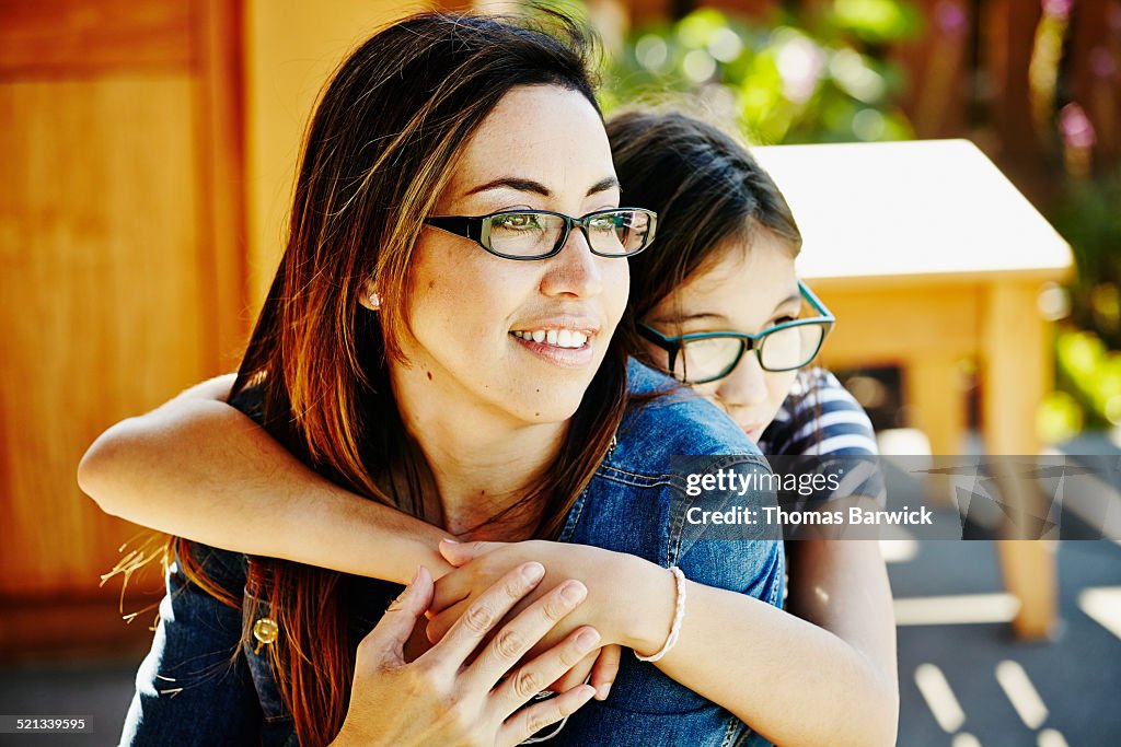 Young daughter embracing smiling mother on patio