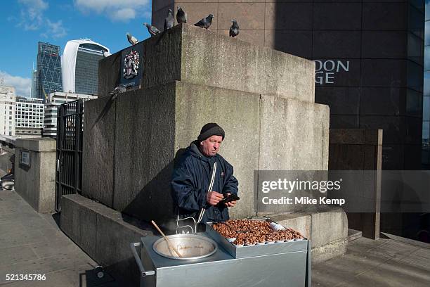 Peanut seller on London Bridge with pigeons lying in wait to eat his savoury treats when he is not looking. London, England, UK. These crafty birds...