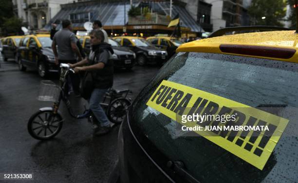 Mand rides his bike next to a cab displaying a banner that reads in Spanish "Get out Uber", while cabs block Callao and Santa Fe avenues during a...