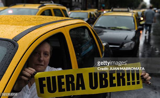 Taxi driver holds a banner reading in Spanish "Get out Uber" while cabs block Callao avenue, during a protest against Uber in Buenos Aires on April...