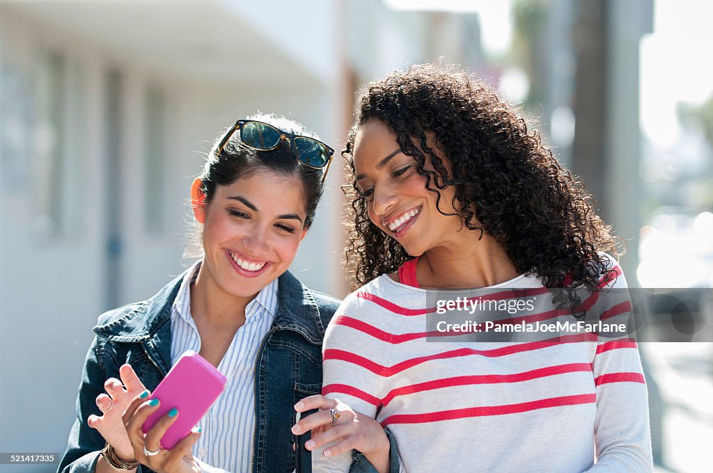 Hispanic und African American Freundinnen Lachen im Mobiltelefon