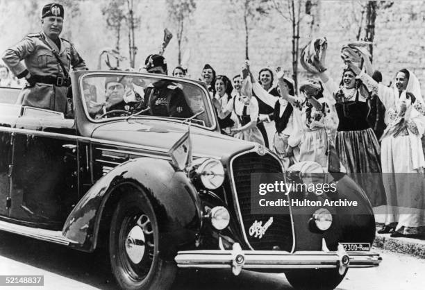 Italian dictator Benito Mussolini is greeted by girls in gala dress during an official visit to Genoa, circa 1935.