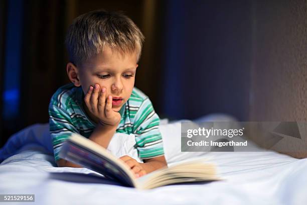 little boy reading book in bed - bedtime story book stock pictures, royalty-free photos & images