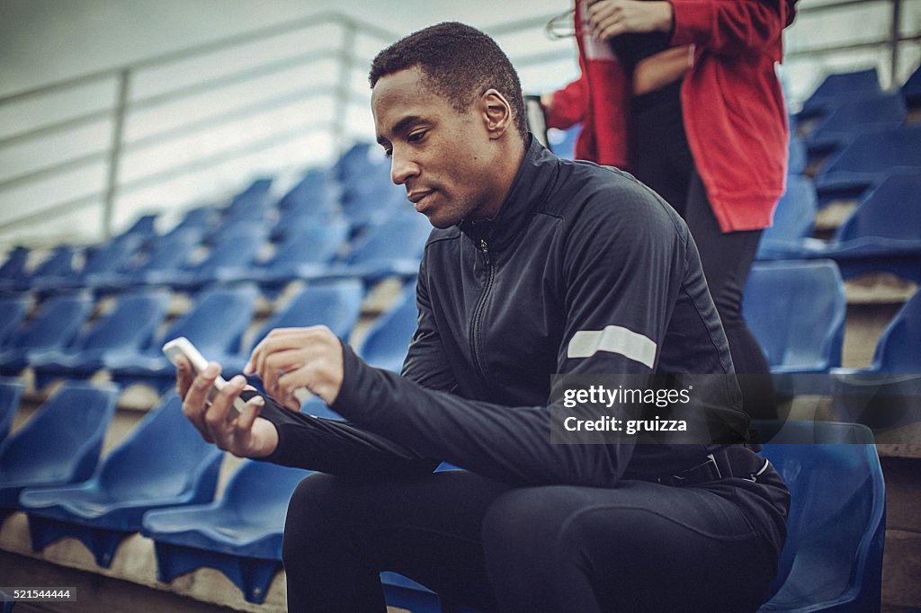 Young fit man texting at the stadium after strenuous workout