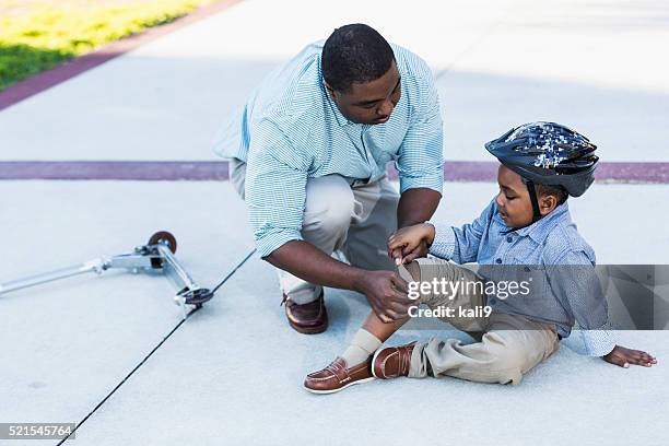 african american father putting bandage on son's knee - human knee stock pictures, royalty-free photos & images