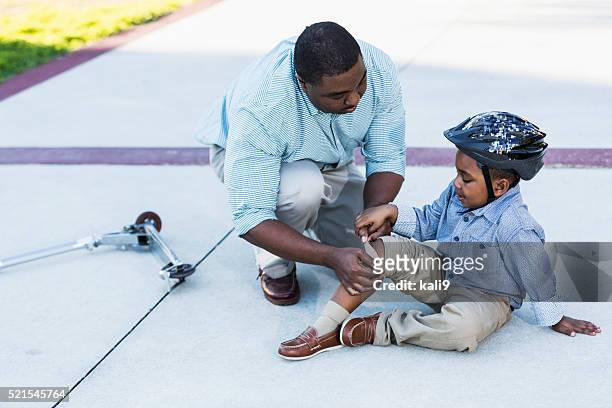 african american father putting bandage on son's knee - knees together 個照片及圖片檔