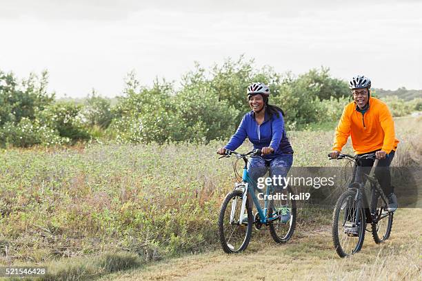 mature african american couple riding bikes in park - adult riding bike through park stockfoto's en -beelden