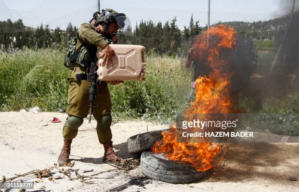 An Israel soldier extinguishes burning tyres set alight by Palestinian demonstrators to create a road block as they throw stones at Israeli cars...