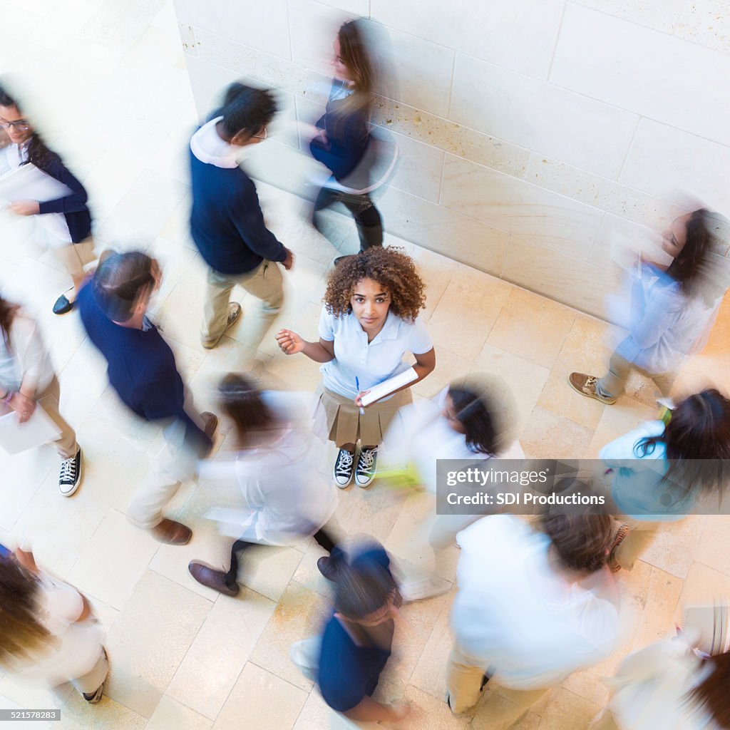 Confused private school student standing in busy crowd of classmates