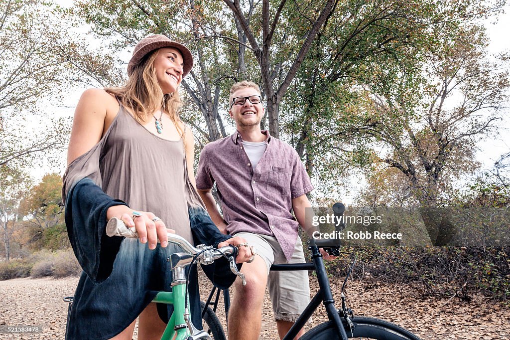 A young, happy man and woman smiling with bicycles in a park for fitness