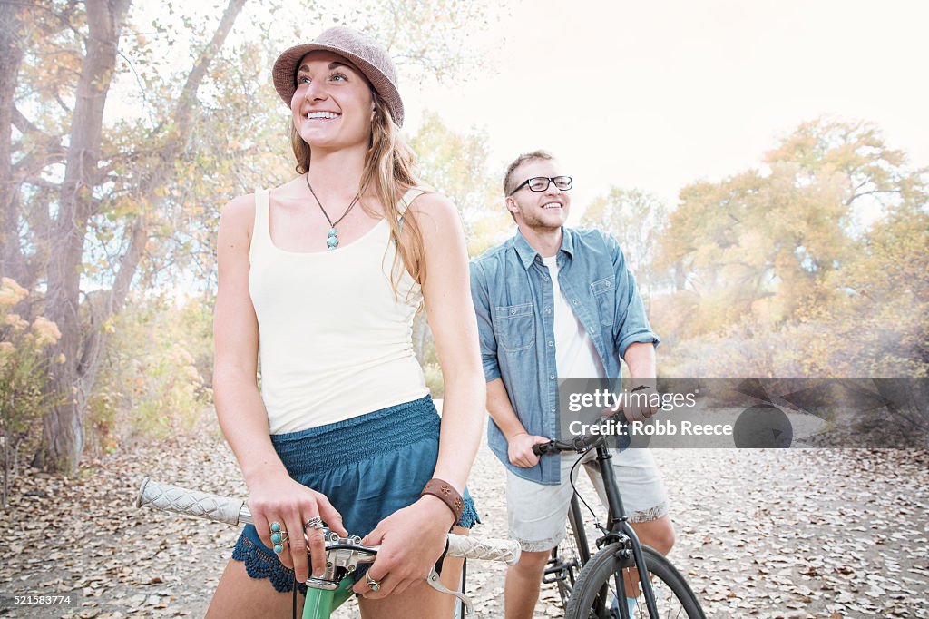 A young, happy man and woman standing with their bicycles in a park