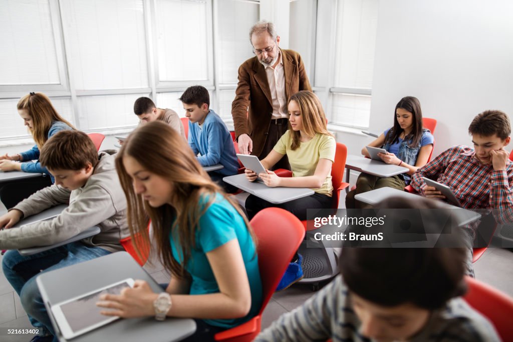 Teacher assisting high school student in a modern classroom.