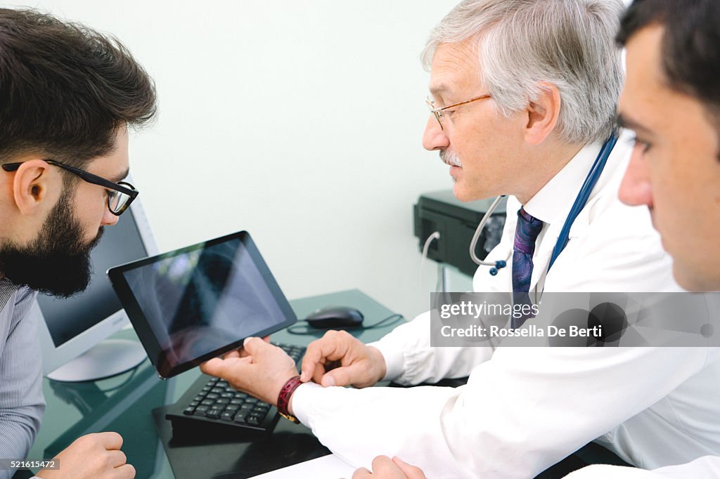 Mature Male Doctor Using A Digital Tablet For His Diagnosis.