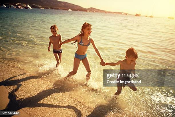 Brothers and sister running on beach laughing