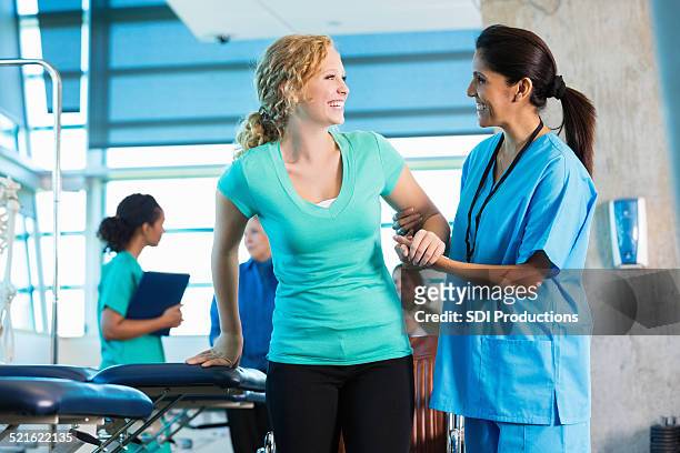 mature physical therapist helping injured teenage girl to walk - injured nurse stock pictures, royalty-free photos & images