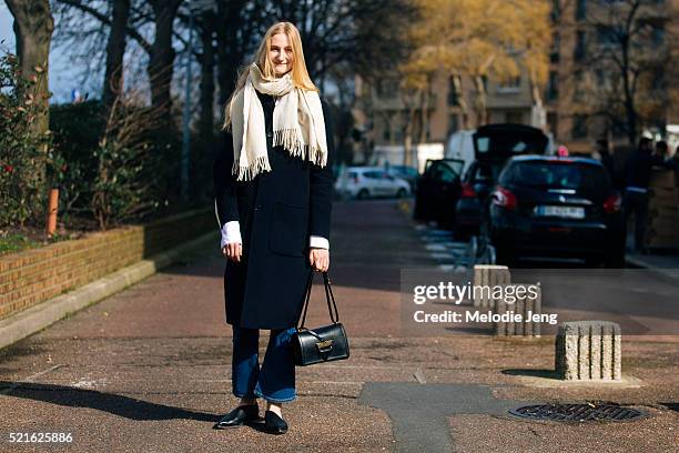 Model Charlotte Lindvig carries a black Loewe bag and wears a white scarf, long black coat, flared jeans, and black loafers after the Balenciaga show...