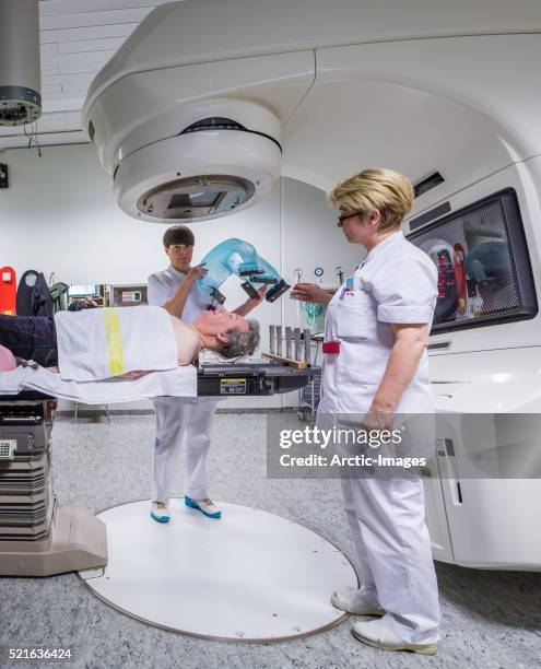nurse technicians positioning plastic mesh mask on male cancer patient for radiation treatment. - particle accelerator stock pictures, royalty-free photos & images