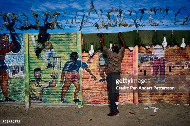 Man hangs rugby shirts that have been laundered on a colorful wall with graffiti in Site C Khayelitsha, a township about 35 kilometers outside Cape...
